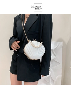 White shell-shaped hard crossbody bag with gold chain strap shown on a model