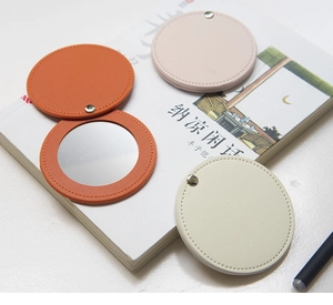 Mini PU leather portable makeup mirrors in orange, beige and pink on desk
