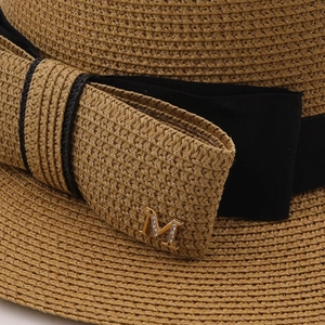 Detailed macro view of beige straw hat with black ribbon bow and rhinestone metal M charm