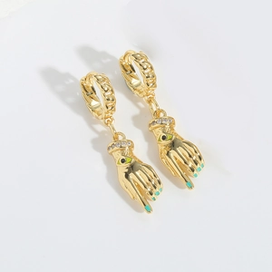 Macro detail of golden palm earrings with green evil eye and textured chain hoop