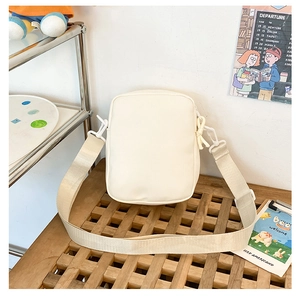White minimalist crossbody bag with adjustable wide strap on a clean wooden display
