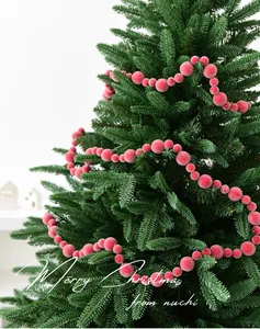 Close-up of red velvet berry garland wrapped on green Christmas tree branches