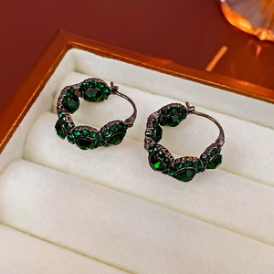 Macro view of vintage emerald-green crystal round hoop earrings on white velvet