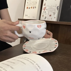 Close-up of handmade ceramic coffee cup with pink heart pattern on a wooden table