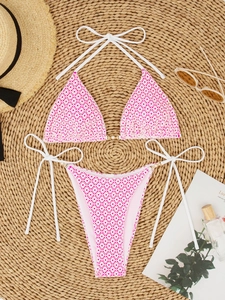 Flat lay of pink geometric bikini with elegant pearl chain straps on a summer beach mat