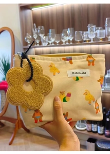 Detail of beige canvas makeup bag with cartoon bear pattern and yellow flower charm