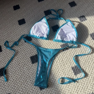 Detail of metallic teal bikini set with gold ring accents and glossy finish on woven rug