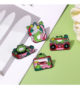 Close-up of cute cartoon frog enamel pins featuring pink musical themes on green background