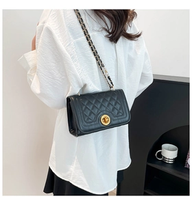 Detail of black quilted shoulder bag featuring a gold chain strap and rotary lock clasp