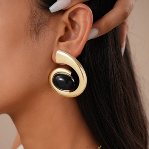 Close-up of model wearing chunky gold metal spiral earrings with a large black oval gemstone