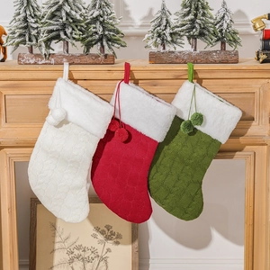 Three knitted Christmas stockings in white, red, and green hanging on a wooden fireplace