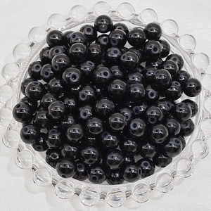 Macro shot of 6mm polished black glass beads piled in a clear glass tray for DIY jewelry