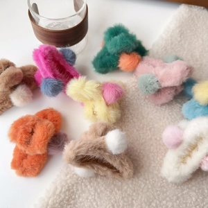 Detail view of colorful plush hair claws with pom-poms on a soft textured background