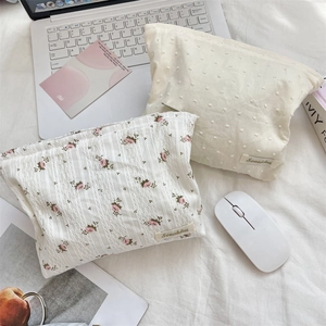 Detail of floral lace and polka dot cosmetic bags with zippers on a white desk setup