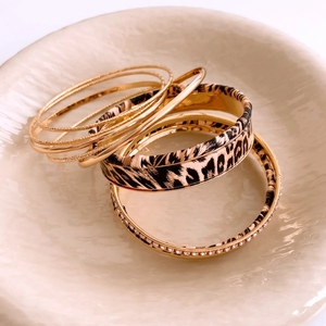 Close-up of stacked leopard print and gold bangles set in a textured beige ceramic bowl