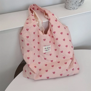 Detailed view of pink canvas tote bag featuring red heart prints and logo tag