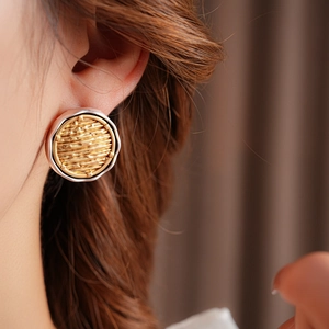 Detail of round earrings featuring a silver outer rim and a golden woven texture inlay