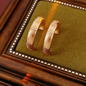 Macro detail of gold flower C-shaped earrings with clear crystals on green velvet