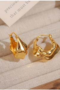 Detail of 18K gold plated V-shaped pleated hoop earrings on a beige linen jewelry tray