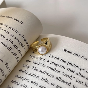 Close-up of a 18k gold pearl ring on an open book, showing refined polished finish