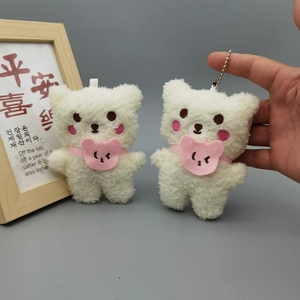 Close-up of white plush bear keychains with pink heart blushes and ribbon details
