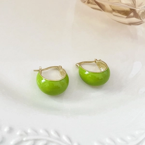 Detail of green enamel C-shaped earrings on a white vintage ceramic plate