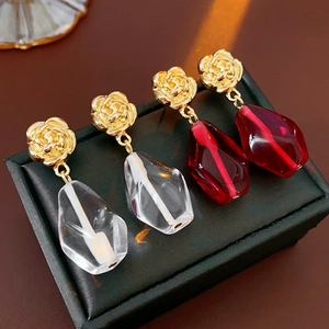Detail of floral gold studs with geometric glass pendants in clear and red crystal tones