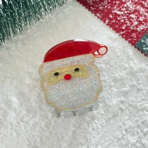 Close-up of a Santa Claus hair claw clip with red glitter hat on a snowy background