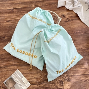 Detail view of mint green drawstring storage bags with gold embroidery on wooden background
