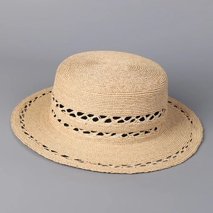 Close-up of hollowed-out hand-woven pattern on a beige flat brim straw beach hat