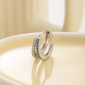 Elegant silver hoop earring with sparkling zircons and blue stones on a beige reflective surface