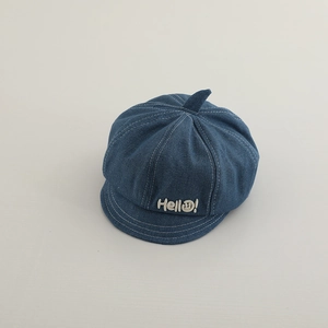 Detail of blue denim newsboy hat featuring white stitching and Hello smile embroidery