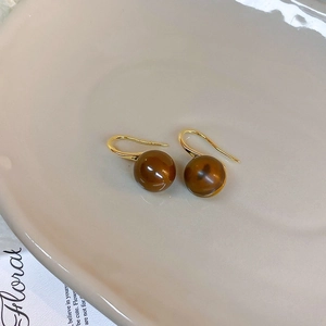 Macro view of geometric brown pearl earrings with gold hooks on a ceramic tray