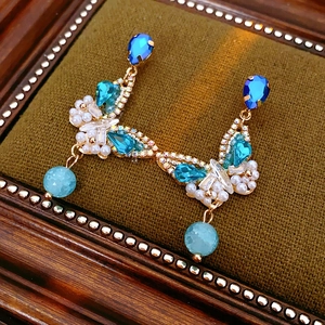 Detail of vintage gold crane earrings with blue crystals and hanging pearl beads
