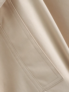 Gros plan du tissu beige du trench montrant le tissage sergé et les doubles coutures