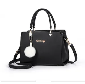 Detail view of black matte leather handbag with gold hardware and white plush charm accessory