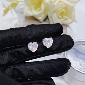 Macro shot of rose gold heart-shaped crystal stud earrings on a black glove