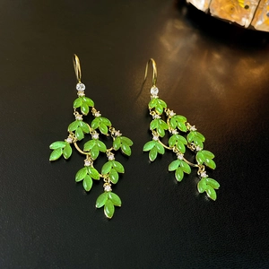 Elegant gold flower earrings with green leaf design and crystals on a dark background