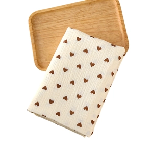Soft beige muslin baby swaddle with brown heart patterns on a wooden tray