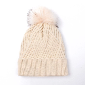 Close-up of cream knit beanie with thick ribbed texture and fluffy faux fur pom-pom