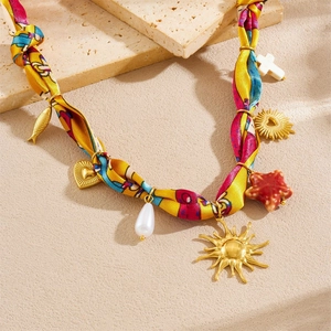 Detail of rope necklace with gold sun, heart, and starfish charms on a textured stone base