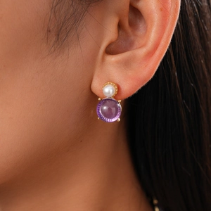 Close-up of pearl and purple gemstone stud earrings with gold plating on ear