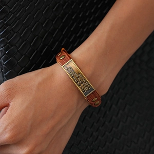 Detail of vintage leather bracelet with bronze metal plate and engraved quote on black background