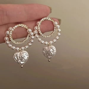 Detail of a vintage heart-shaped pearl earring with gold rhinestones held by hand