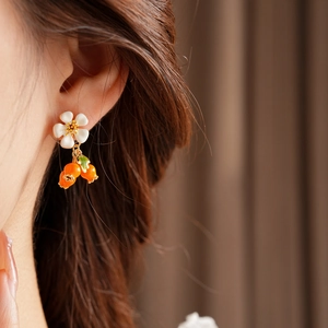 Close-up of vintage flower earrings with orange berry charms on female model's ear