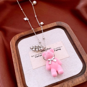 Detailed close-up of pink flocked bear pendant with pearls on a wooden display