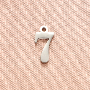 Macro view of polished stainless steel number 7 pendant on pink textured fabric background
