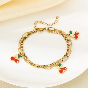 Macro detail of gold double-layer chain bracelet featuring red cherry charms on white ceramic