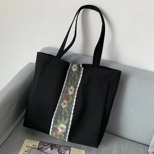 Dettaglio ricamo floreale su borsa tote in tela nera appoggiata su un divano grigio