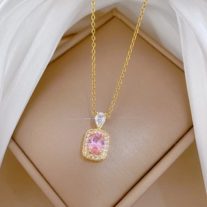 Macro detail of a gold necklace featuring a pink oval pendant set on white silk fabric